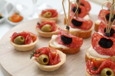 Photo of Many different tasty canapes on wooden board, closeup