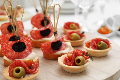 Photo of Many different tasty canapes on wooden board, closeup