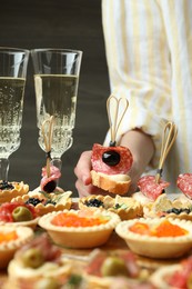 Photo of Woman taking tasty canape at table, closeup