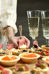 Photo of Woman taking tasty canape at table, closeup