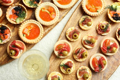 Photo of Many different tasty canapes and wine on white table, flat lay