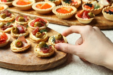 Photo of Woman taking tasty canape at white table, closeup