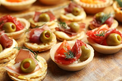 Photo of Many different tasty canapes on wooden board, closeup