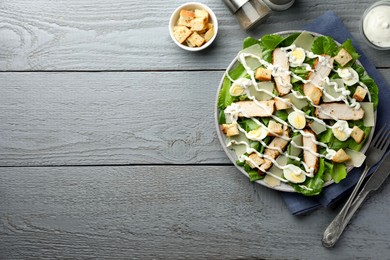 Photo of Delicious Caesar salad with chicken served on grey wooden table, flat lay. Space for text