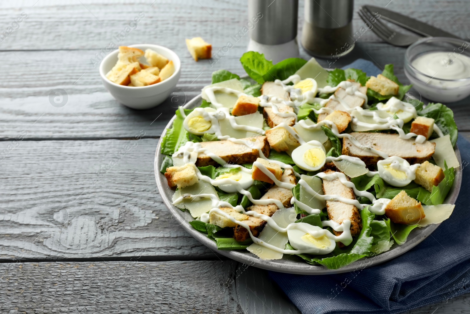 Photo of Delicious Caesar salad with chicken on grey wooden table, closeup. Space for text