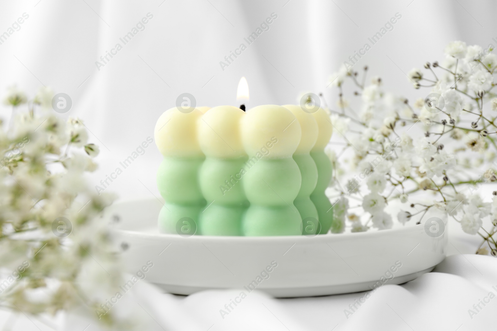 Photo of Stylish bubble candle and gypsophila flowers on white cloth, closeup