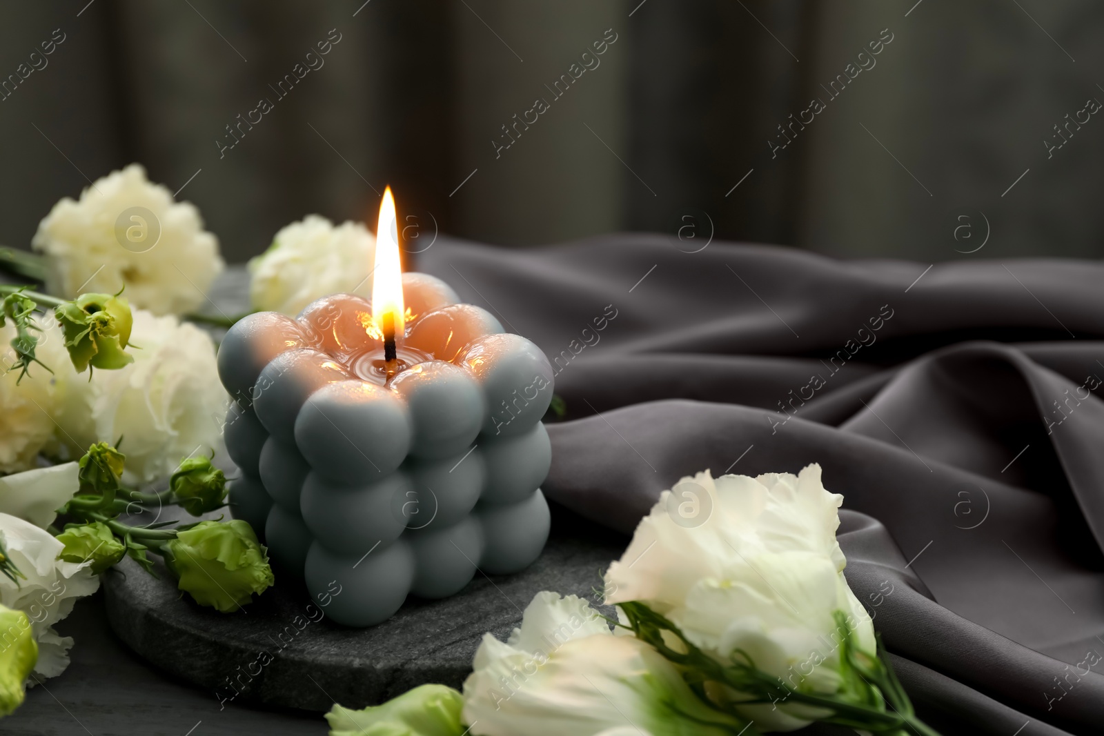 Photo of Burning bubble candle and beautiful flowers on table, closeup