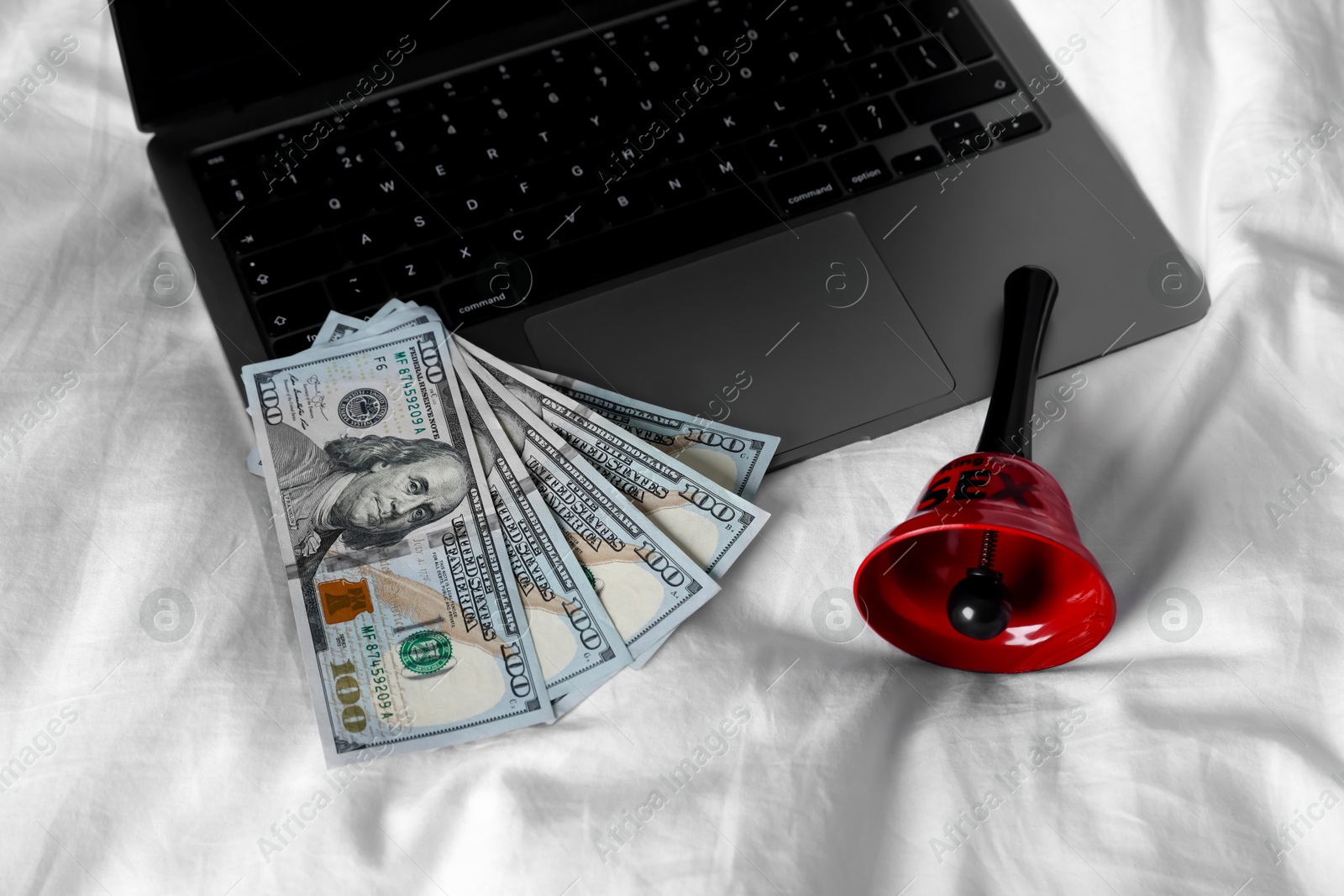 Photo of Prostitution and virtual sex. Laptop, dollar banknotes and bell on linens