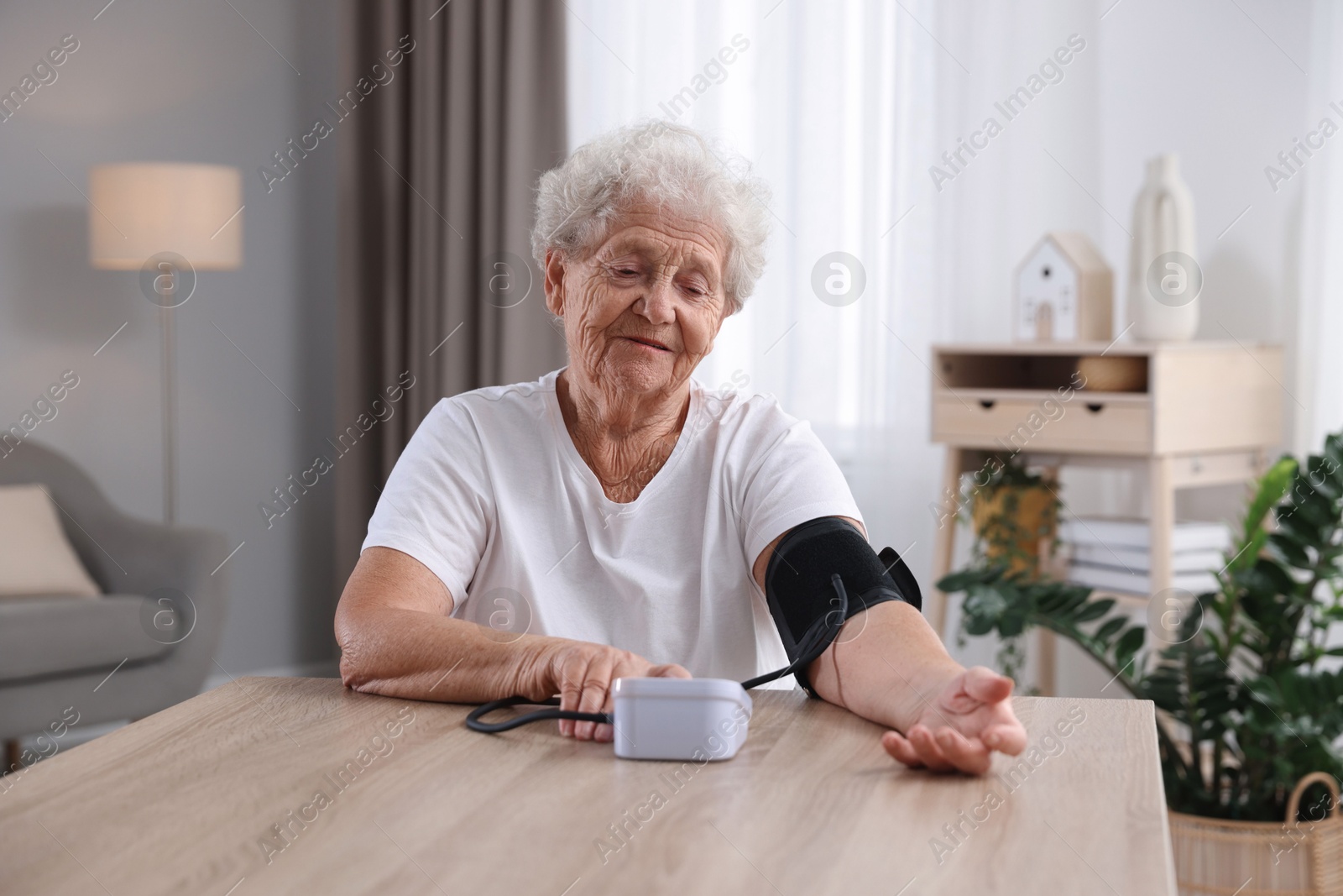 Photo of Senior woman measuring blood pressure at wooden table indoors