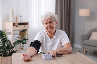 Photo of Senior woman measuring blood pressure at wooden table indoors