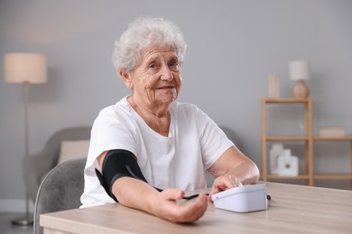 Photo of Senior woman measuring blood pressure at wooden table indoors