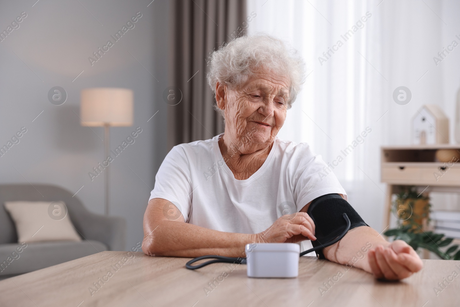 Photo of Senior woman measuring blood pressure at wooden table indoors