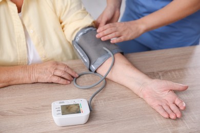 Photo of Healthcare worker measuring patient's blood pressure at wooden table indoors, closeup