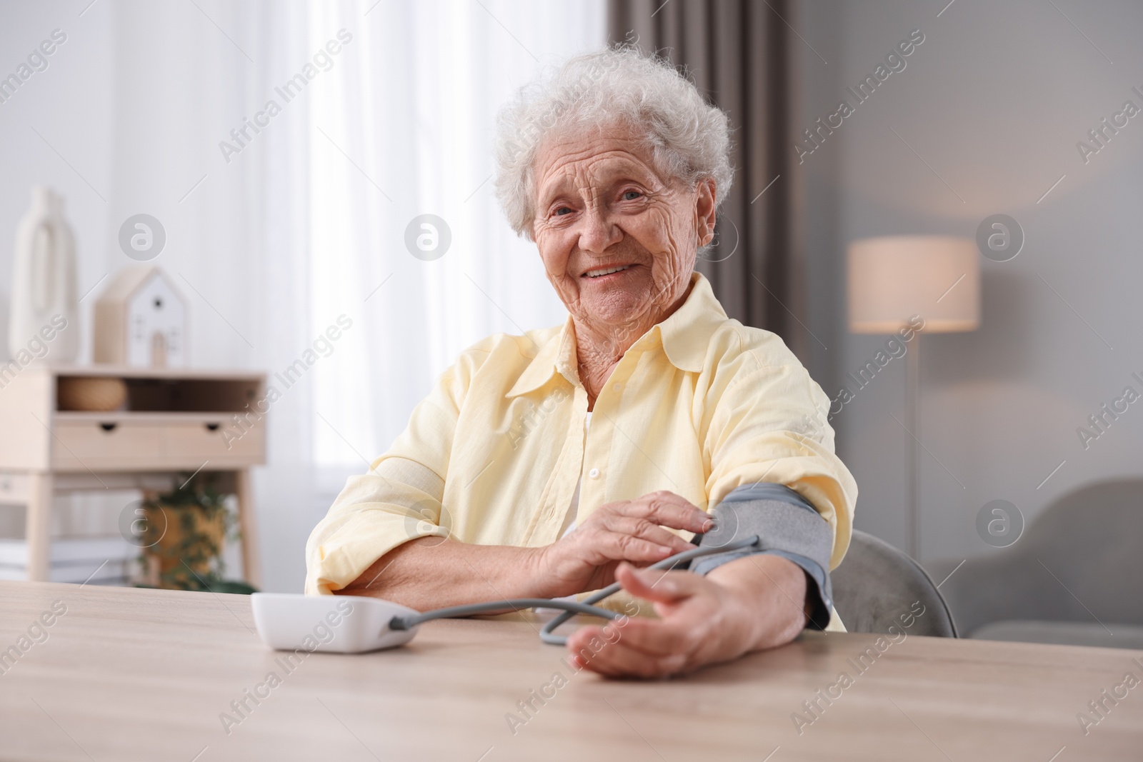 Photo of Senior woman measuring blood pressure at wooden table indoors