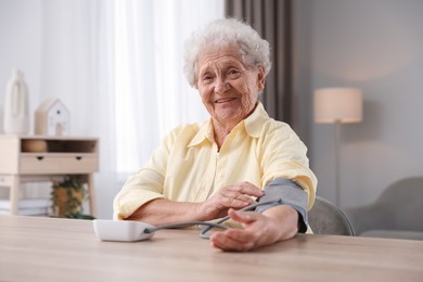 Photo of Senior woman measuring blood pressure at wooden table indoors