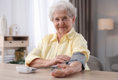 Photo of Senior woman measuring blood pressure at wooden table indoors