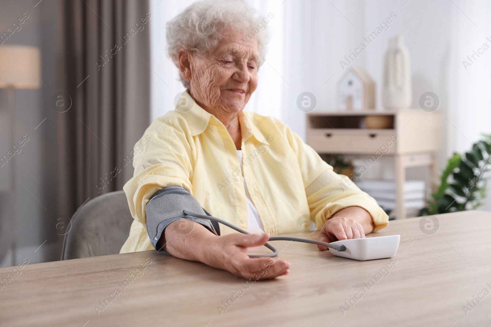 Photo of Senior woman measuring blood pressure at wooden table indoors