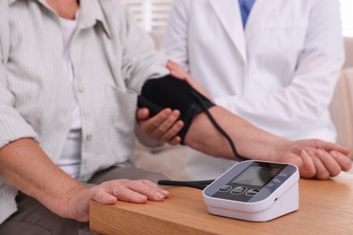 Photo of Doctor measuring patient's blood pressure at wooden table indoors, closeup