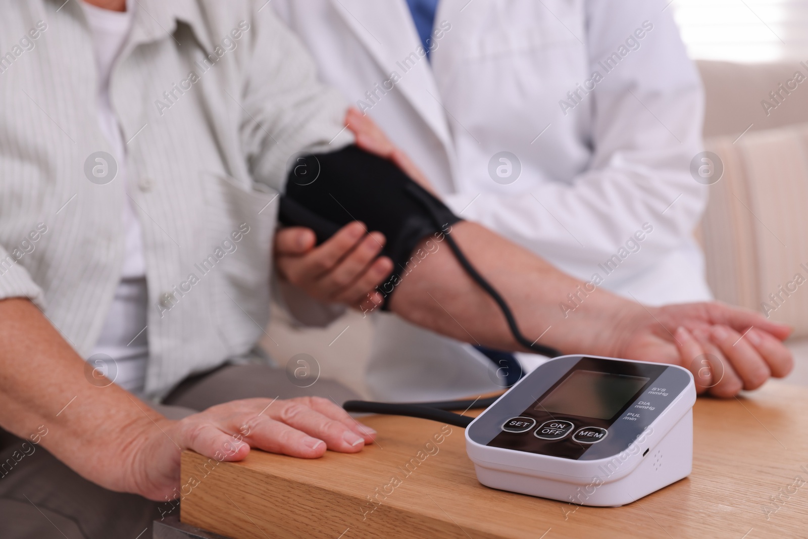 Photo of Doctor measuring patient's blood pressure at wooden table indoors, closeup