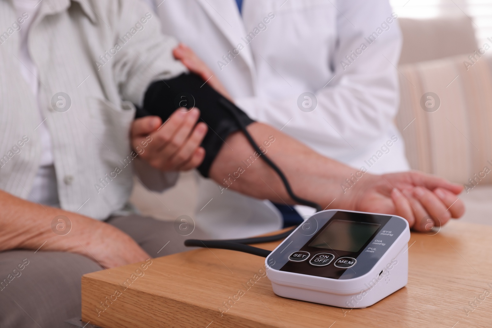 Photo of Doctor measuring patient's blood pressure at wooden table indoors, closeup