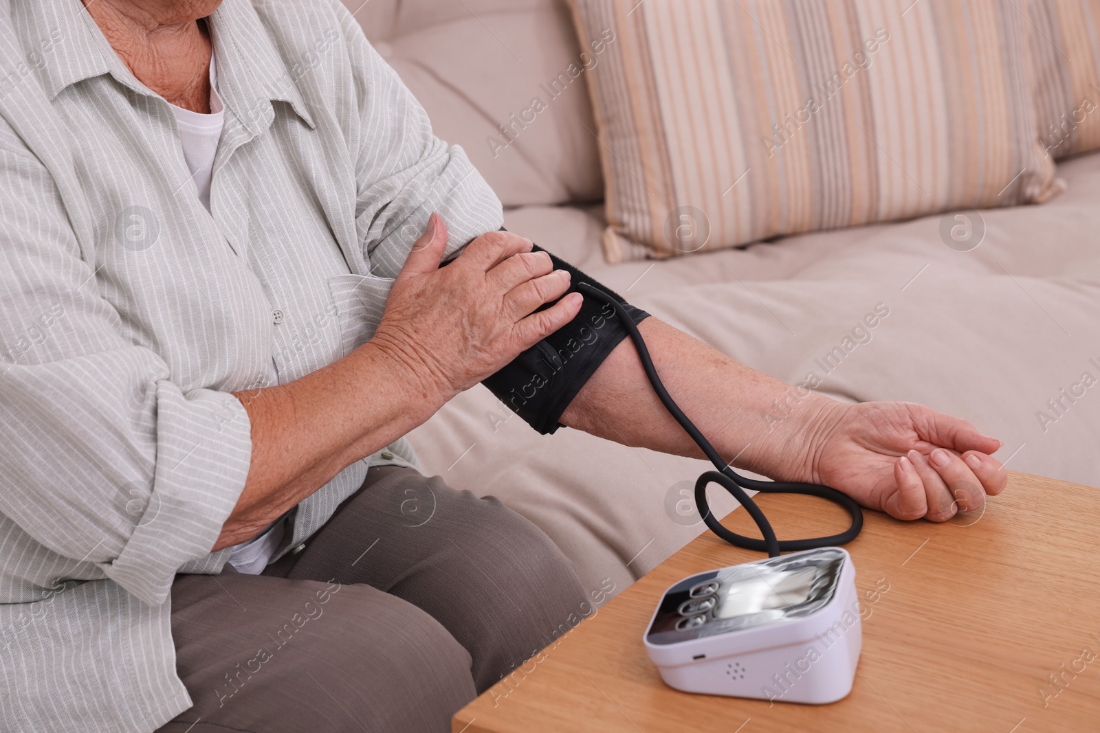 Photo of Senior woman measuring blood pressure at wooden table indoors, closeup