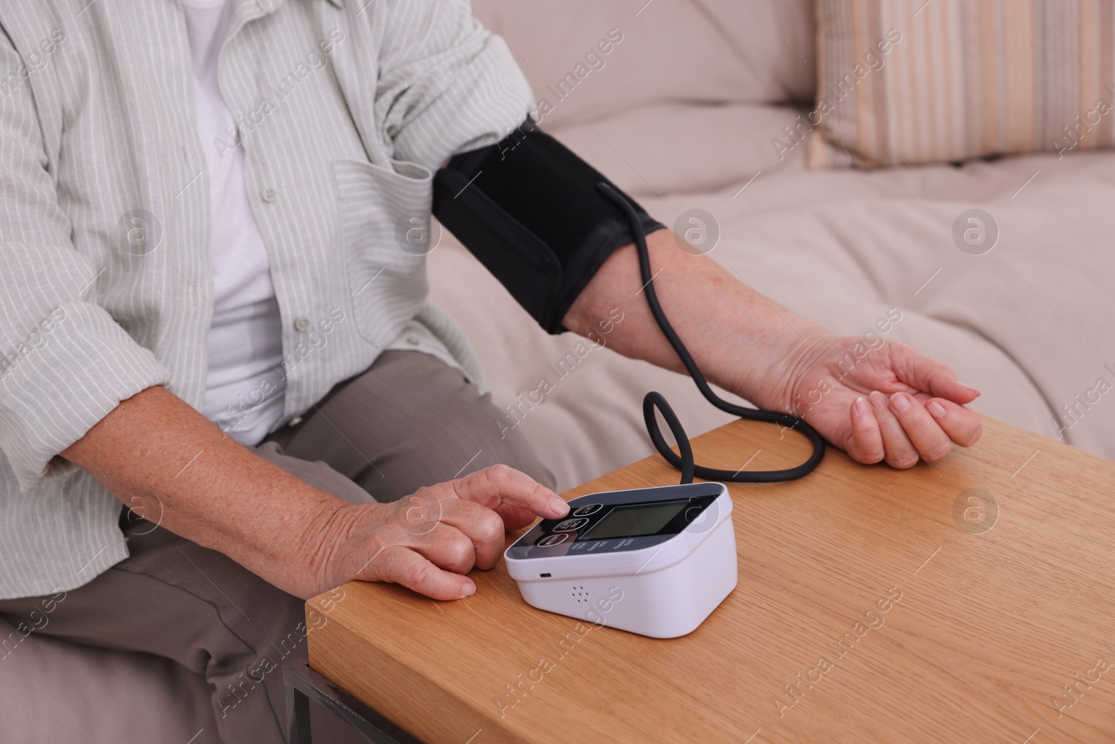 Photo of Senior woman measuring blood pressure at wooden table indoors, closeup