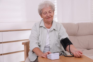 Photo of Senior woman measuring blood pressure at wooden table indoors