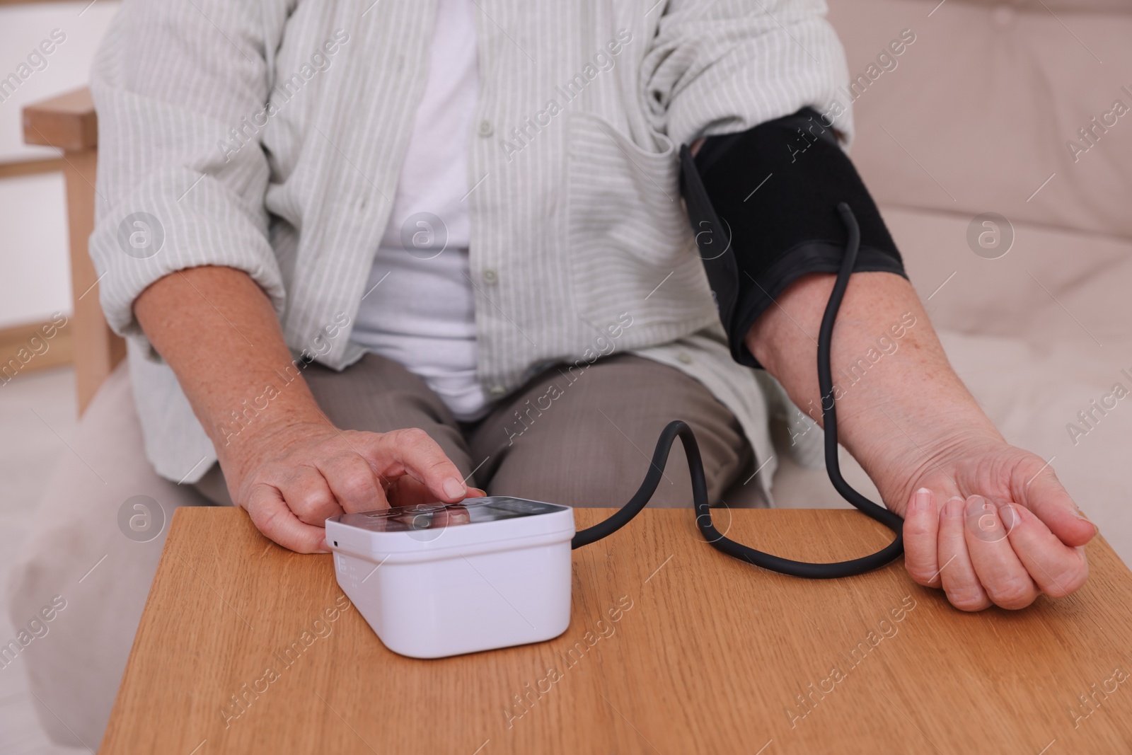 Photo of Senior woman measuring blood pressure at wooden table indoors, closeup