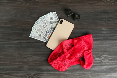 Photo of Sex work. Smartphone, underwear, dice and money on wooden surface, flat lay