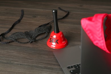 Photo of Sex work. Bell, mask and laptop on wooden surface, selective focus