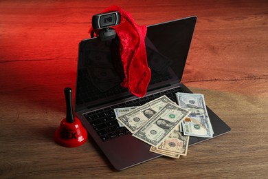 Photo of Sex work. Laptop with web camera, panties, bell and money on wooden surface