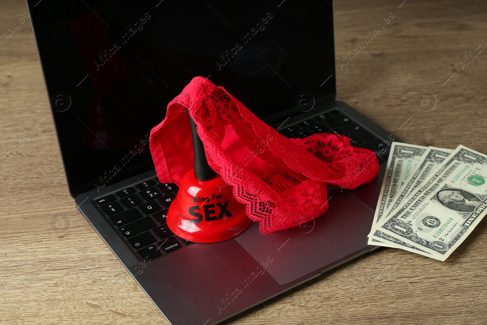 Photo of Sex work. Laptop with lingerie, bell and money on wooden surface