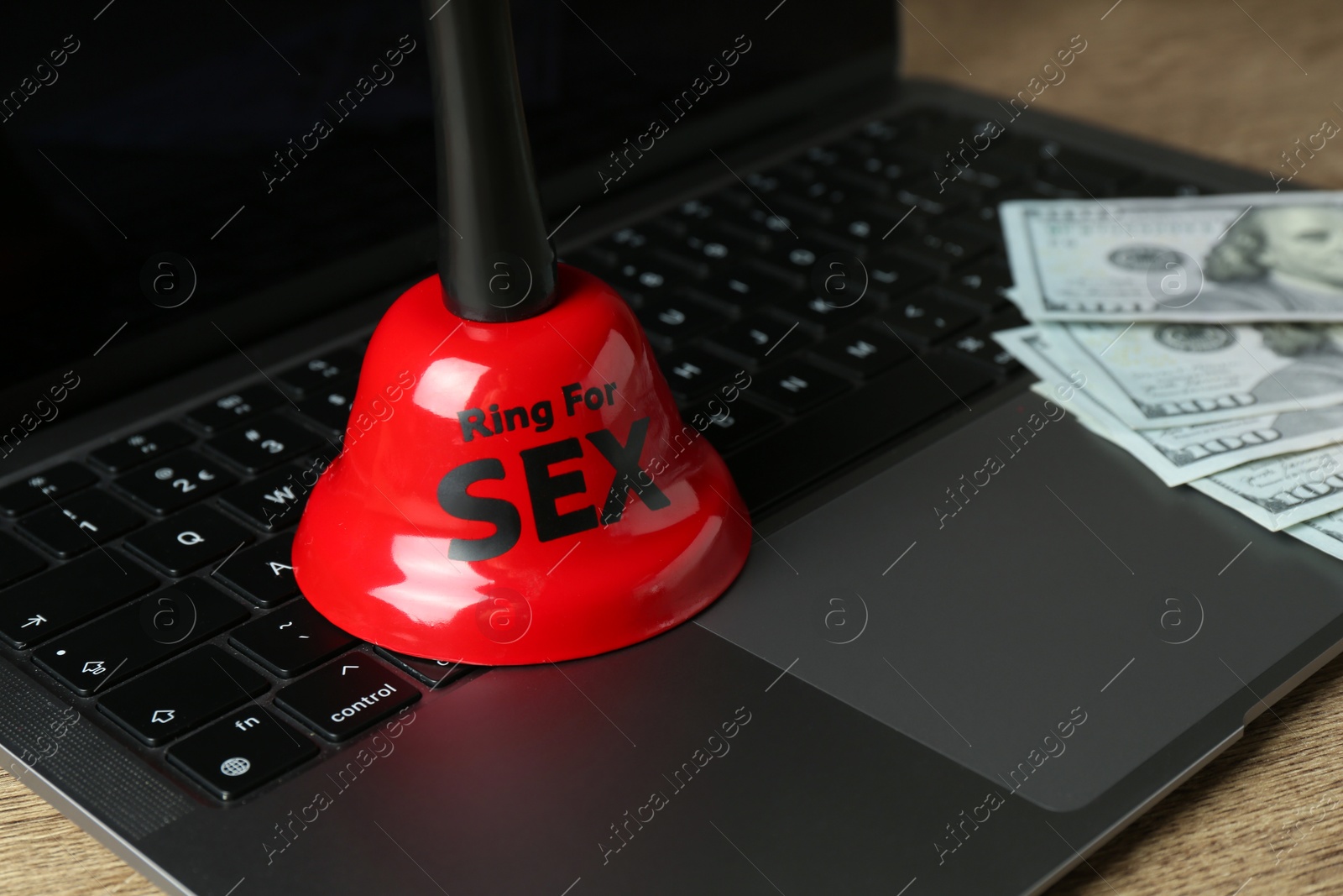 Photo of Sex work. Laptop with bell and money on wooden surface, closeup