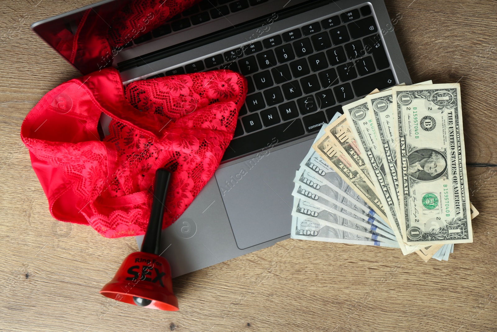 Photo of Sex work. Laptop with bell, underwear and money on wooden surface, top view