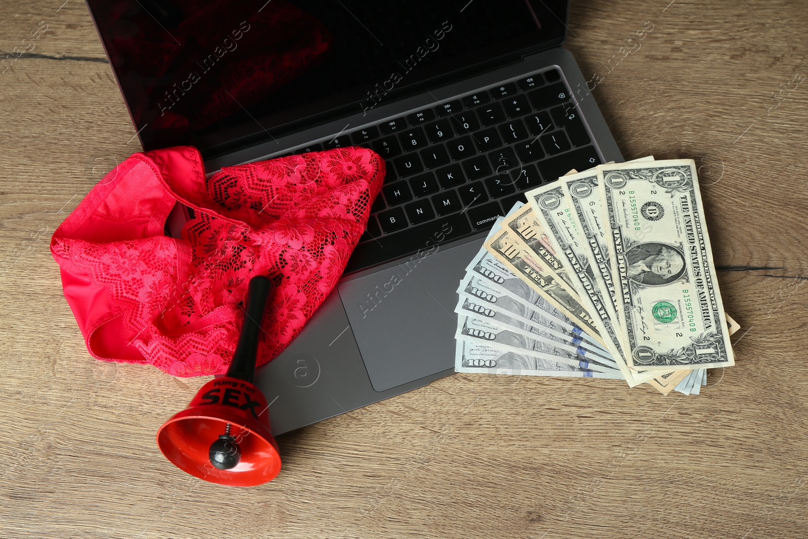 Photo of Sex work. Laptop with bell, underwear and money on wooden surface, above view