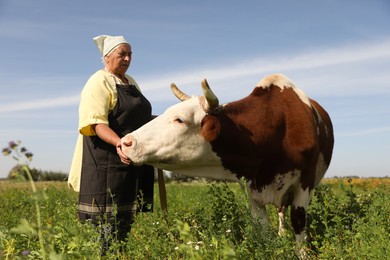 Photo of Senior woman with beautiful cow on pasture