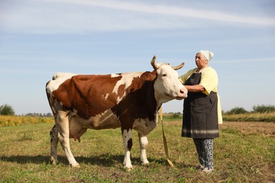 Photo of Senior woman with beautiful cow on pasture