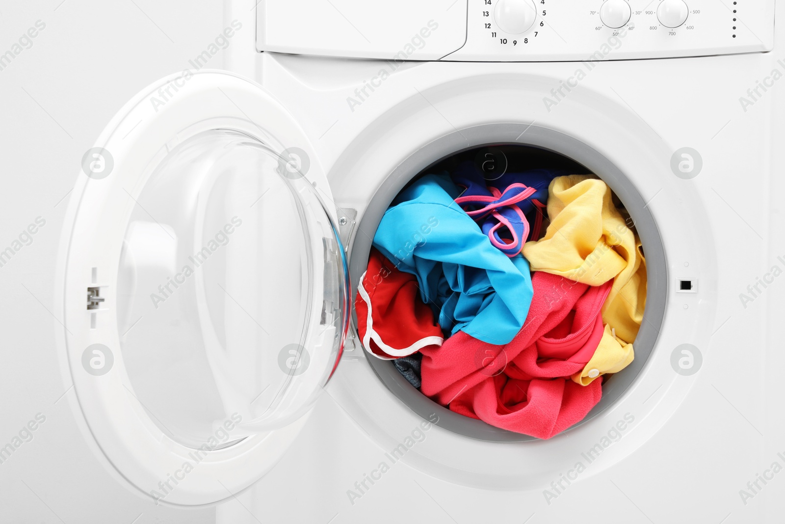 Photo of Washing machine with laundry near light wall, closeup