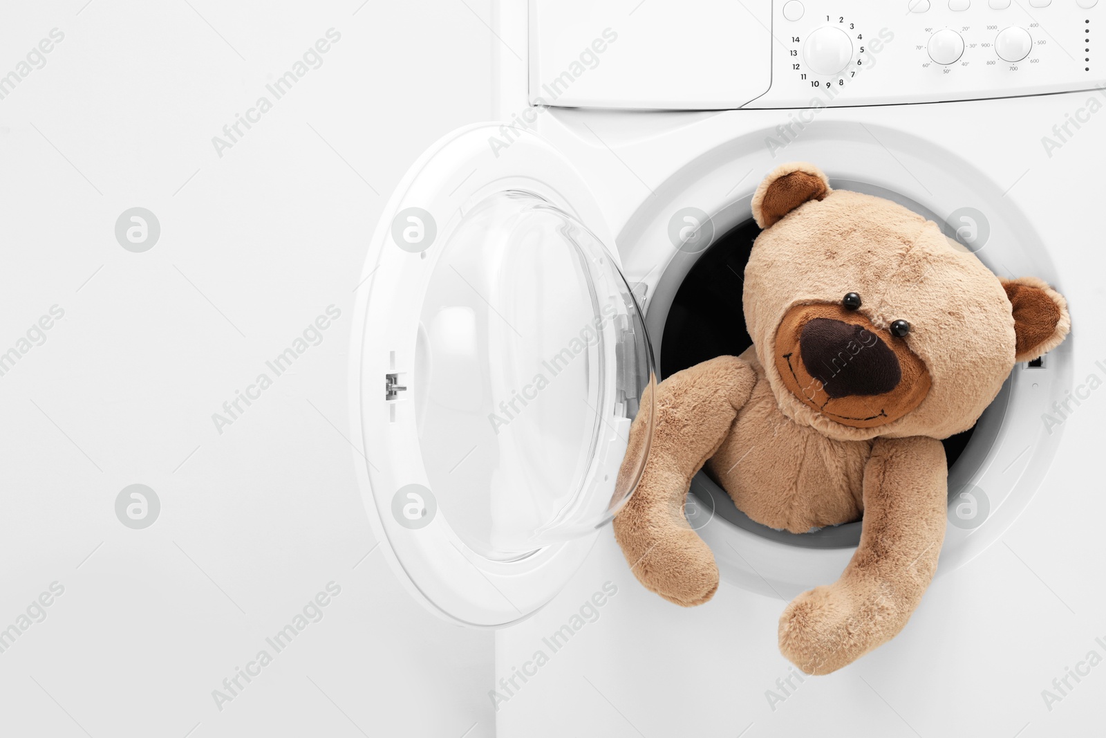 Photo of Washing machine with teddy bear near light wall, space for text