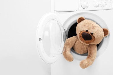 Photo of Washing machine with teddy bear near light wall, space for text