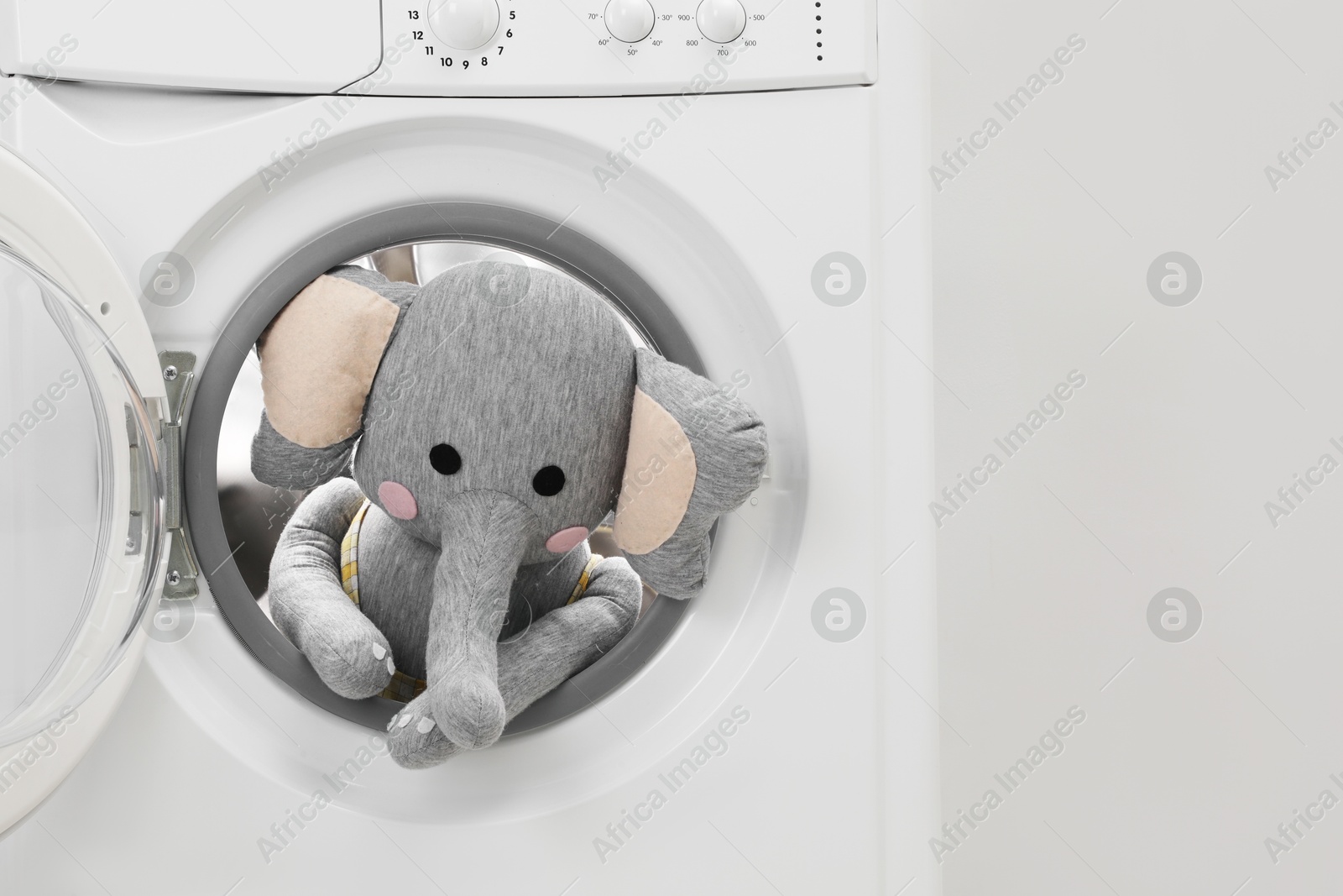 Photo of Washing machine with toy elephant near light wall, closeup