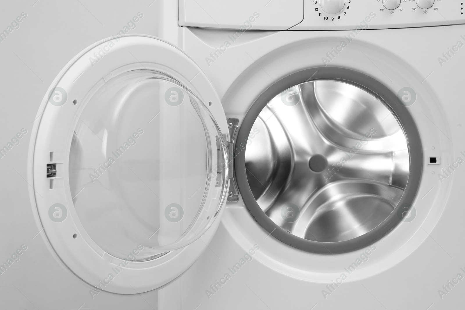 Photo of Washing machine with empty drum near light wall, closeup