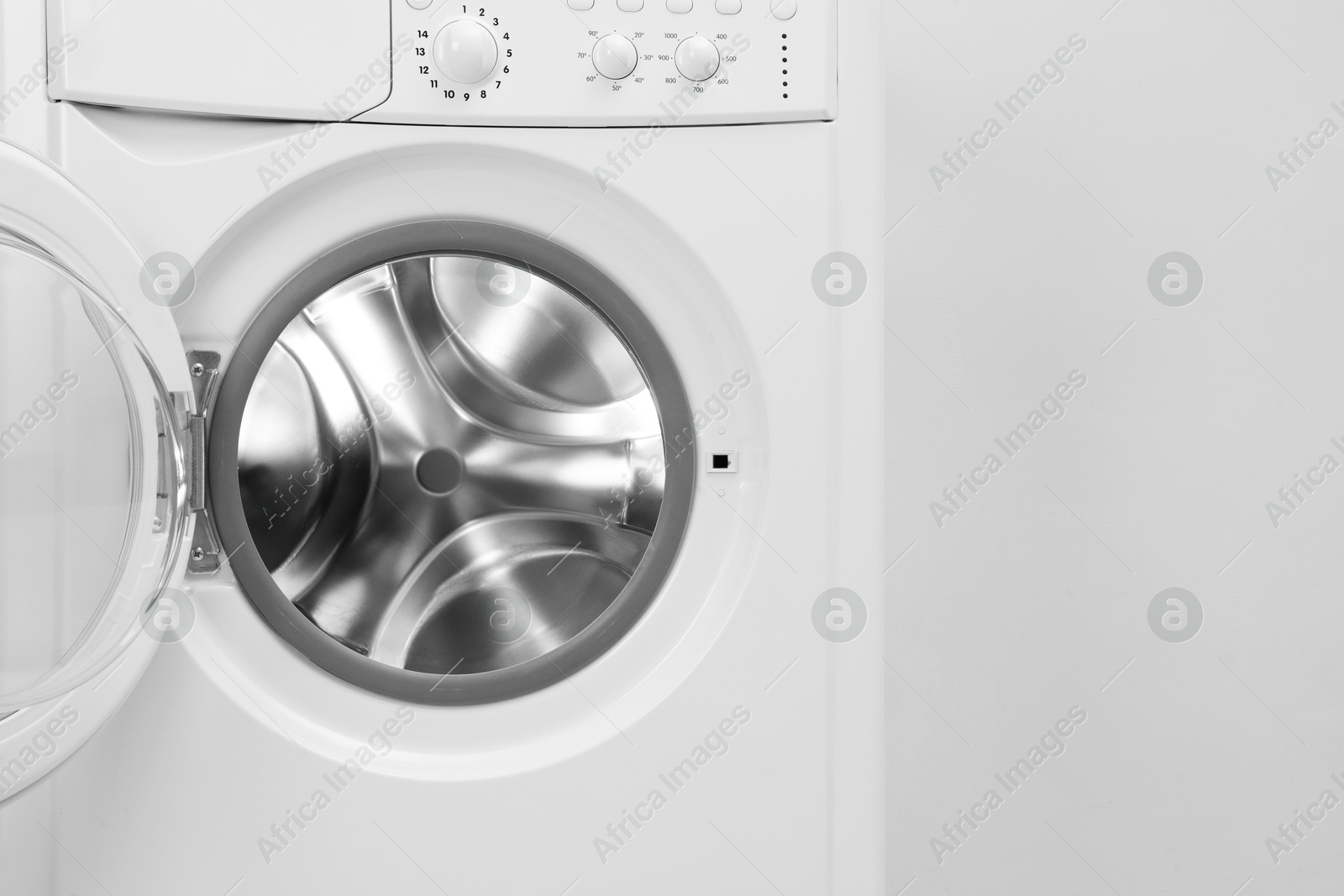 Photo of Washing machine with empty drum near light wall, closeup. Space for text