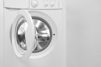 Photo of Washing machine with empty drum near light wall, closeup. Space for text