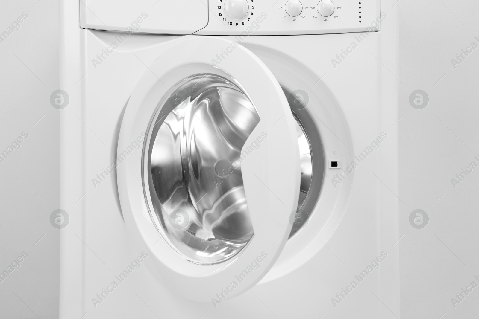 Photo of Washing machine with empty drum near light wall, closeup