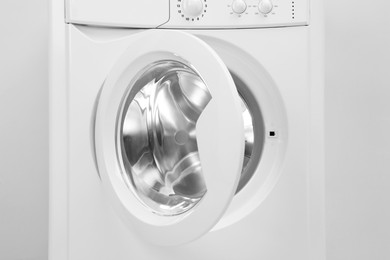 Photo of Washing machine with empty drum near light wall, closeup