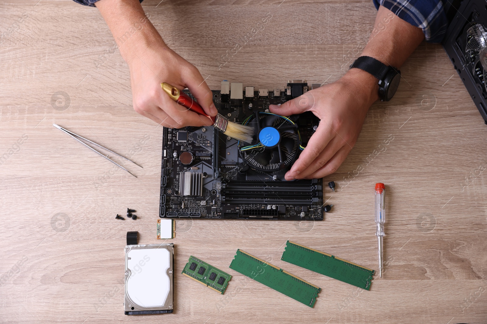 Photo of Man cleaning motherboard with computer chip at wooden table, top view