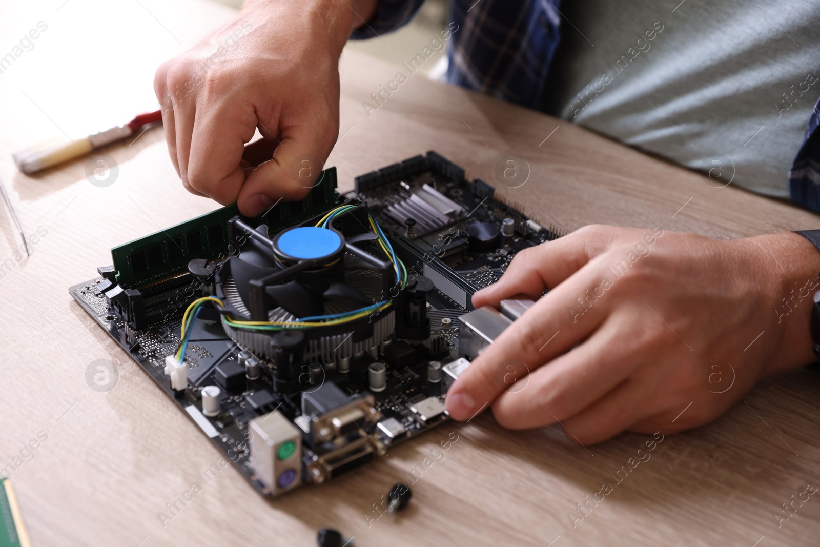 Photo of Man installing computer chip onto motherboard at wooden table, closeup