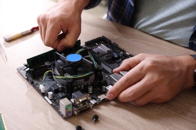 Photo of Man installing computer chip onto motherboard at wooden table, closeup