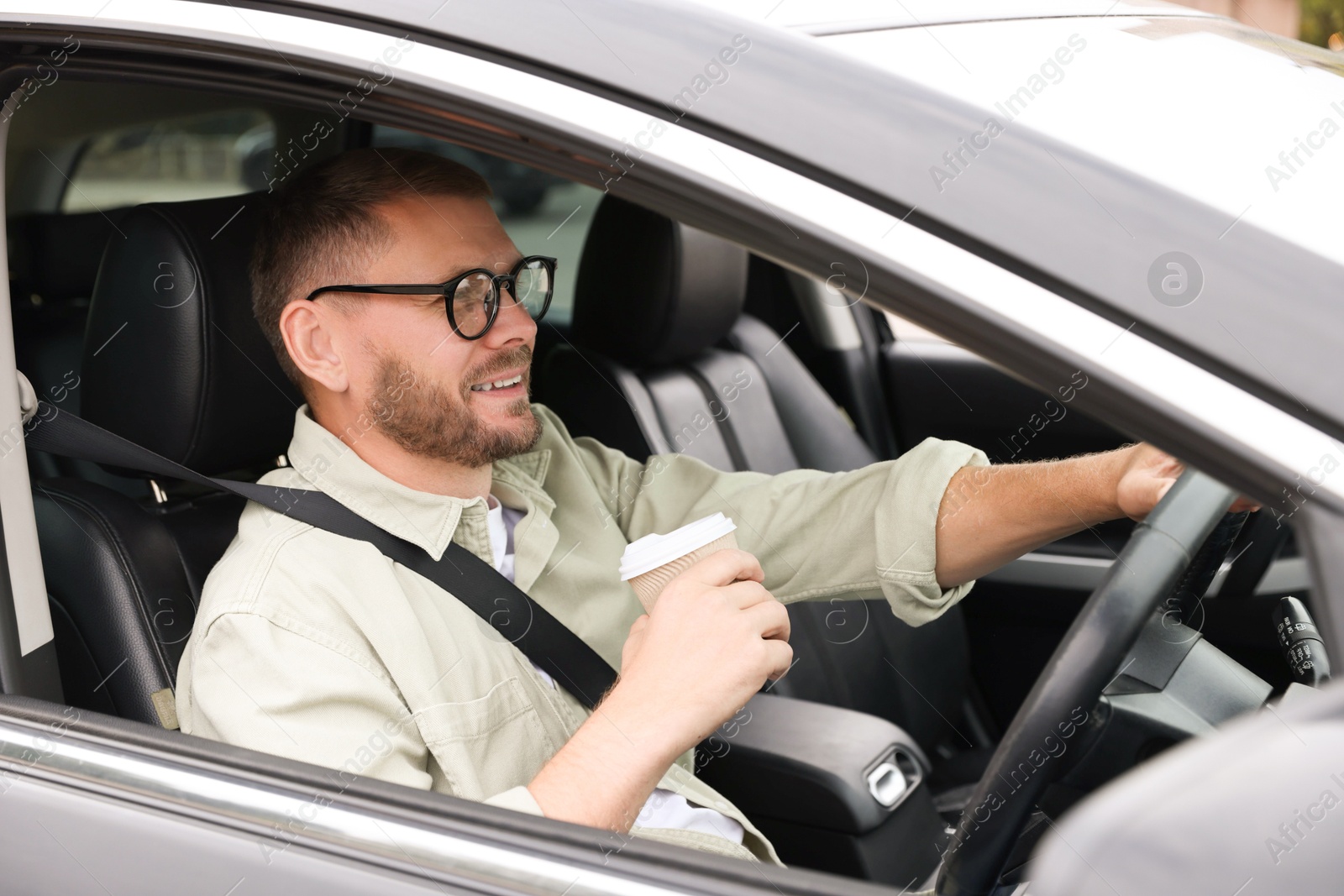 Photo of Man with cup of coffee driving modern car